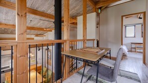 Un intérieur en bois comprenant une table et des chaises, un banc, et donnant sur une pièce avec un lit et une fenêtre.