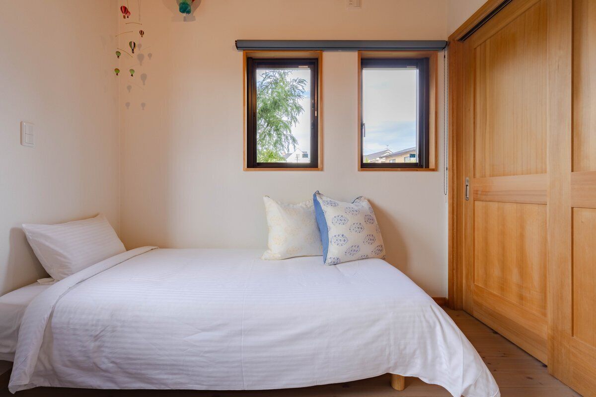 A bedroom with a bed, two windows, a wardrobe, and a wall-mounted light fixture.