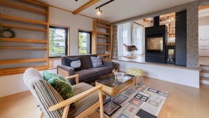 Un salon moderne avec un canapé, un fauteuil et une table basse. On y trouve une cheminée et une fenêtre donnant sur l’extérieur.