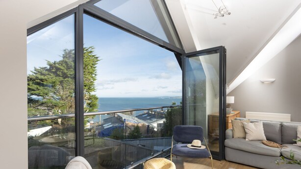 A modern living room with a large glass wall offering a view of the sea and trees. - Cloud 10 St Ives - Sea Views - Free parking & WiFi - Pets Welcome (St Ives)