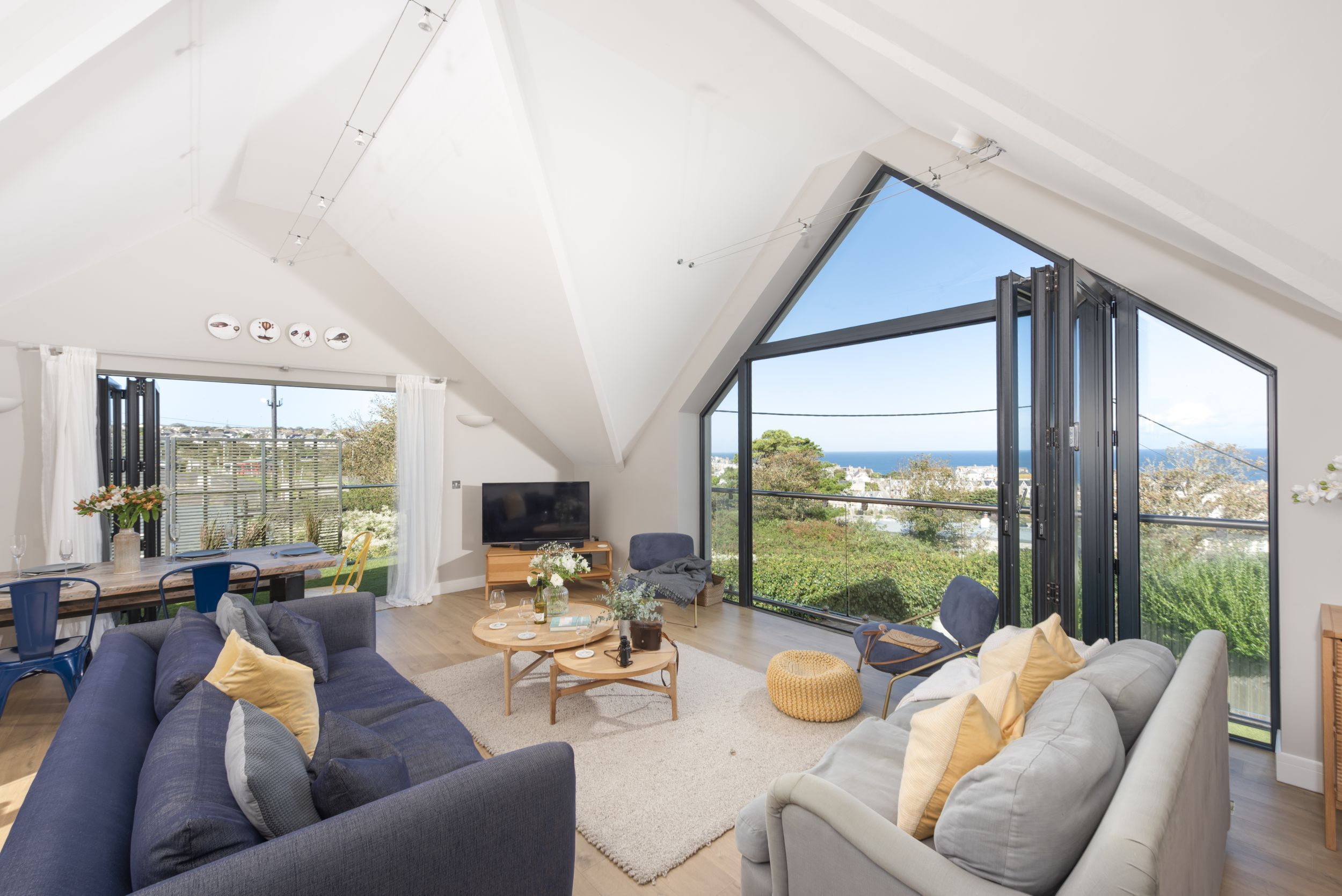 A spacious living area with a high ceiling, a large TV, and a dining table set for two.