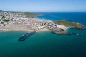 An aerial view of a coastal town with a beach, rocky outcrops, and a fortified structure. - Cloud 10 St Ives - Sea Views - Free parking & WiFi - Pets Welcome (St Ives)