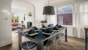 A dining area with a modern table and chairs, a large window with curtains, and a view of a brick building outside. - NFL Spacious Green Lake Home, Dog OK, BBQ/Karaoke (Seattle)