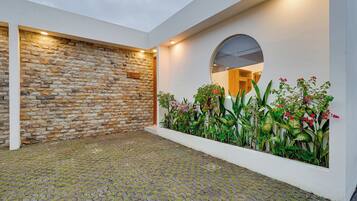 A courtyard with a cobblestone floor, a stone wall, and a planter with various plants and flowers.