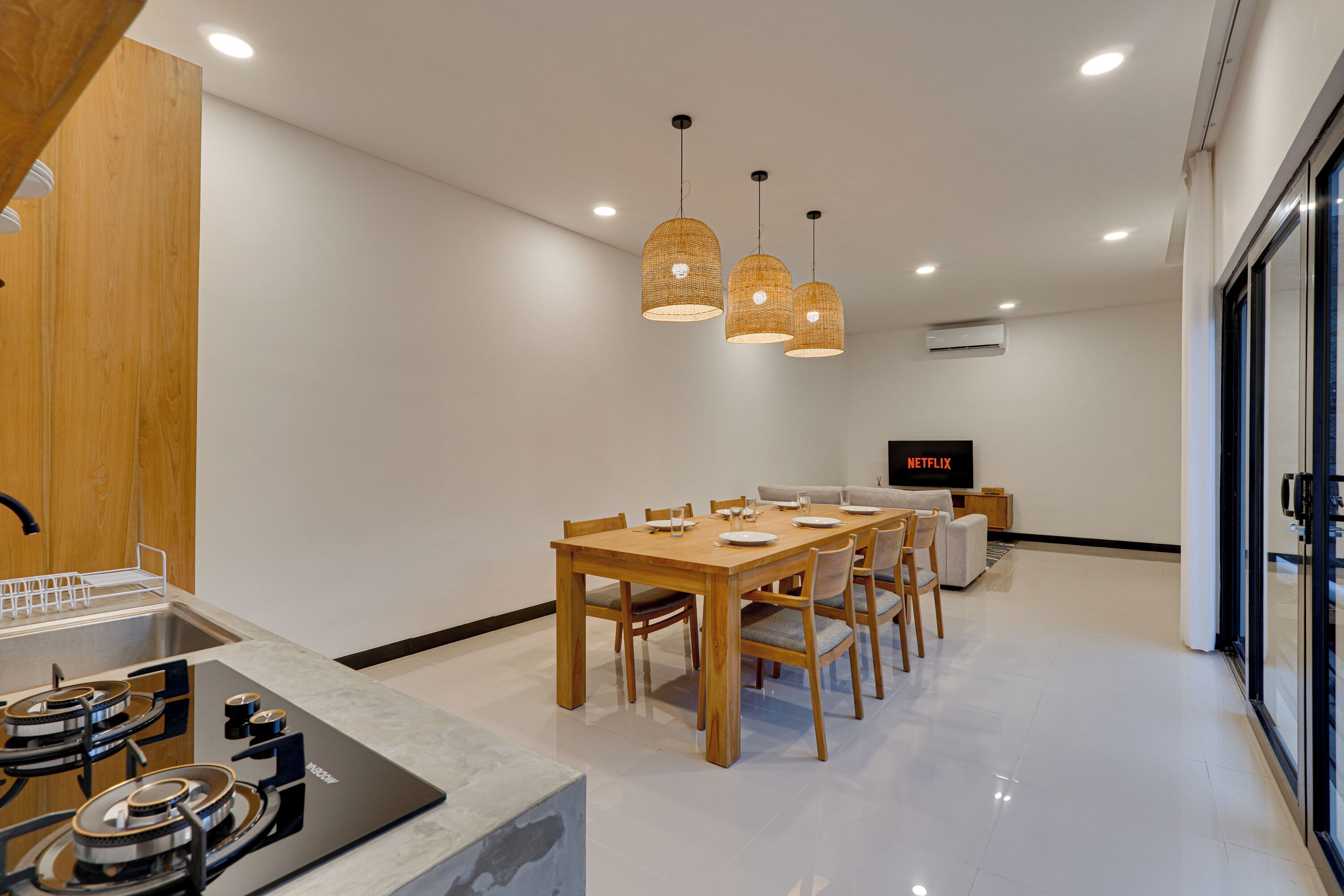 A modern kitchen with a built-in stove, wooden dining table, and hanging pendant lights.