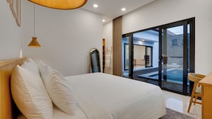 A modern bedroom with a large bed, a wooden desk, and a glass door leading to a balcony. - Bhatara Villa Sanur (Denpasar)