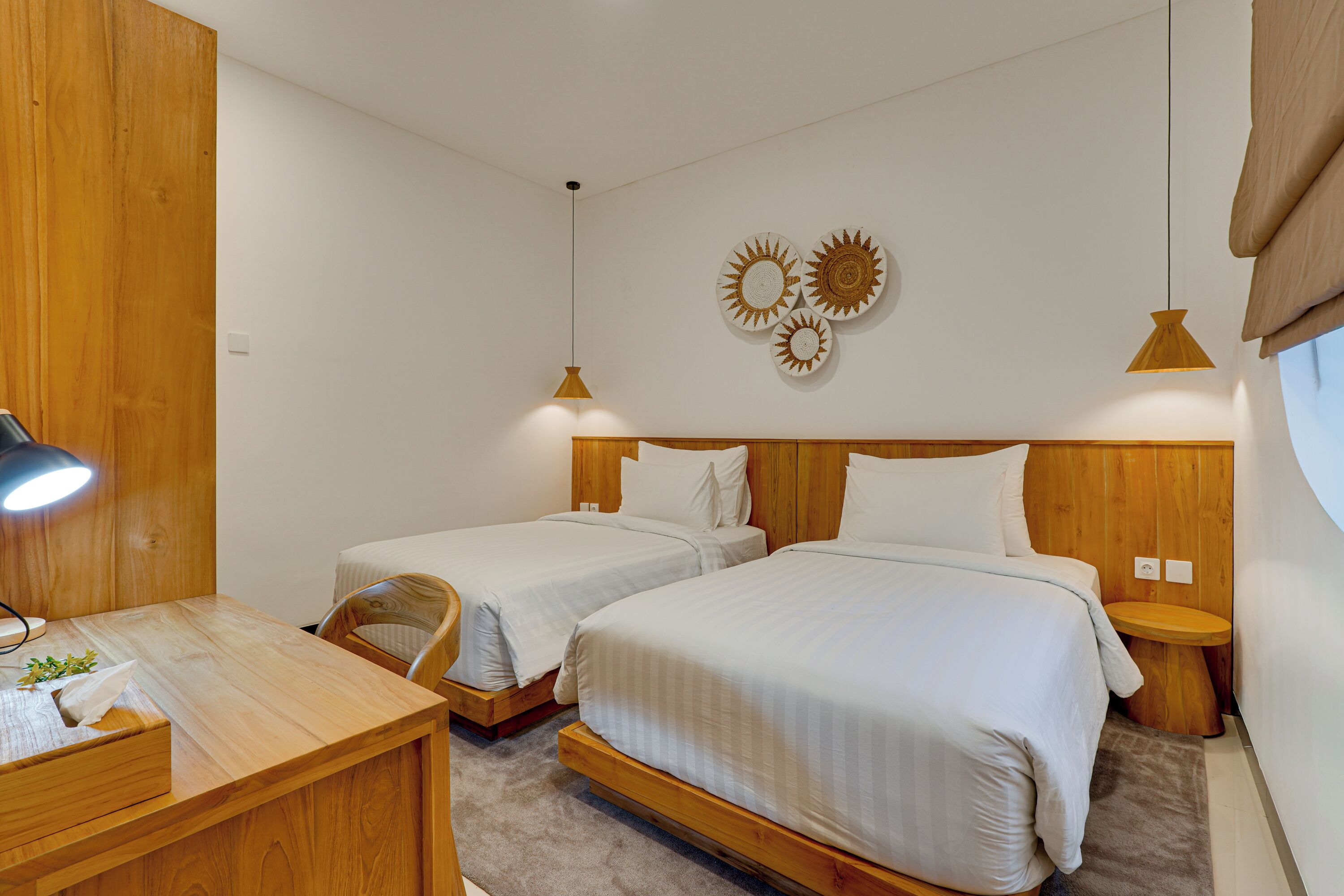 A hotel room with two single beds, a wooden desk with a lamp, and a small table with a tissue box.