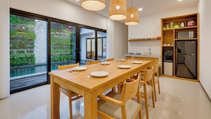 A modern kitchen with a dining area, large windows, and a view of greenery. - Bhatara Villa Sanur (Denpasar)