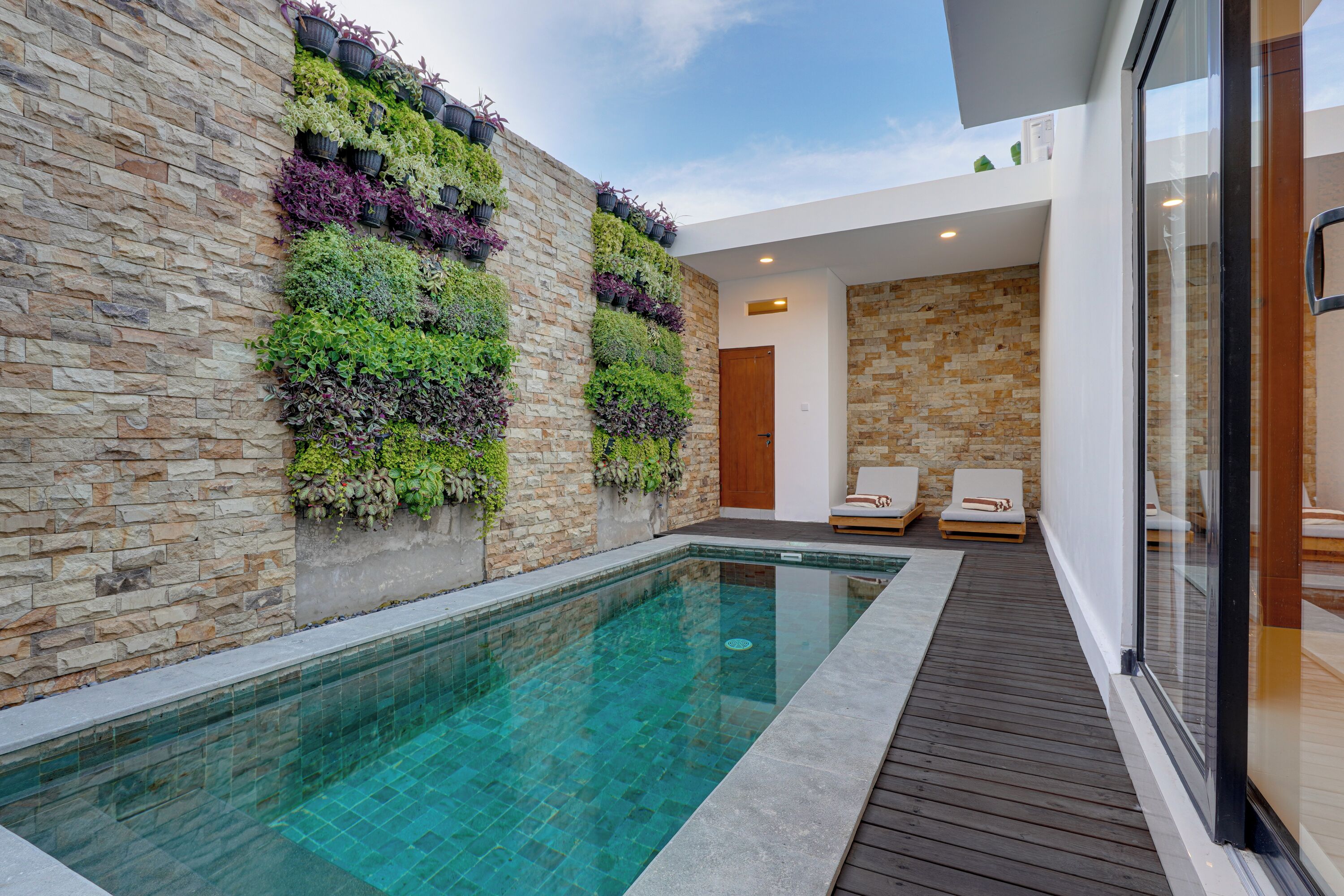 A modern pool area with a stone wall and a wooden deck.