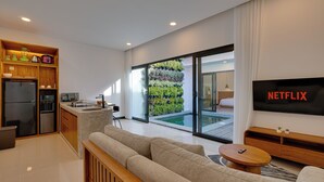 A modern living room with a sofa, a coffee table, and a TV displaying 'NETFLIX'. - Bhatara Villa Sanur (Denpasar)
