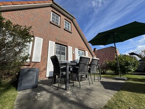 Et murstenshus med terrasse, havemøbler og en stor parasol.