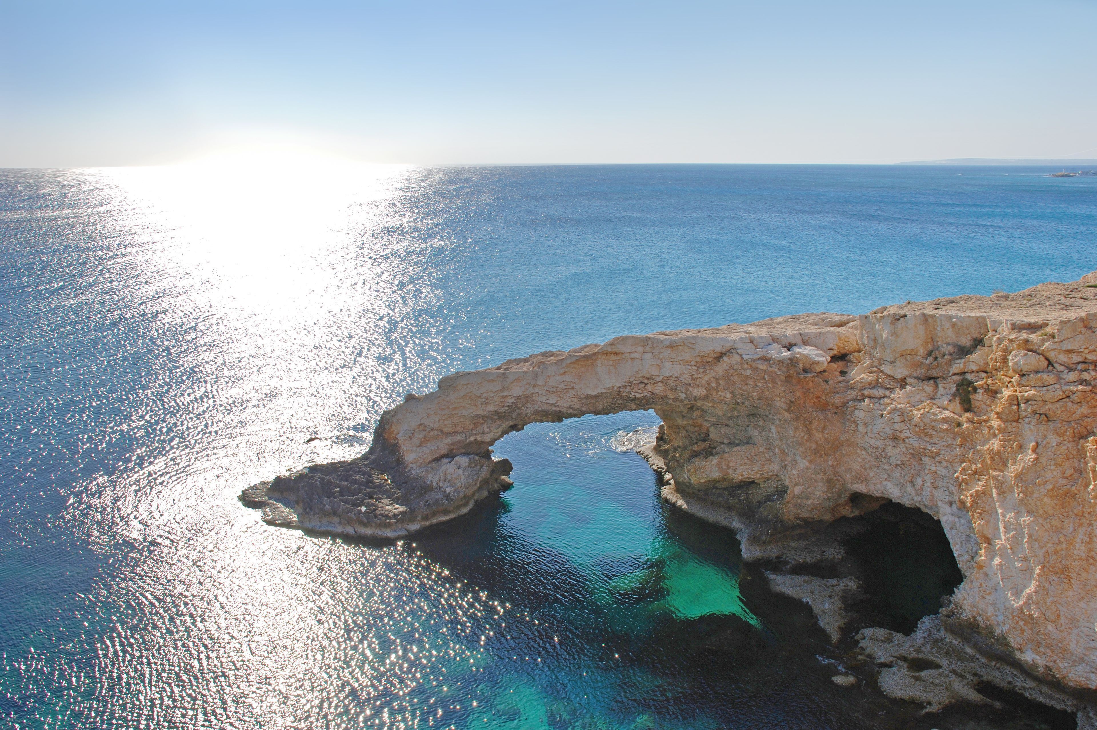 A coastal view with a natural rock formation arching over the sea, providing a sheltered area.