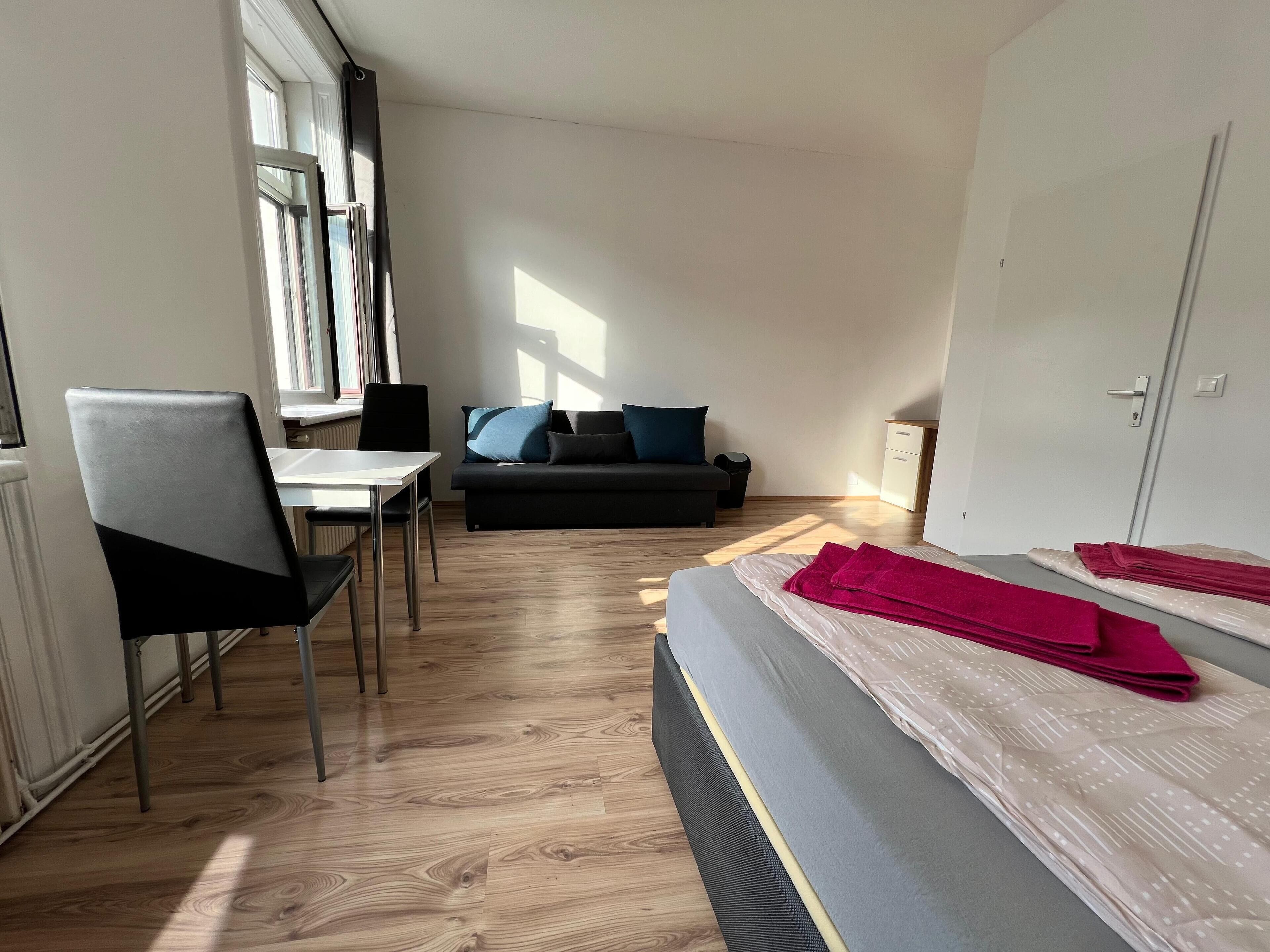 Et værelse med seng, skrivebord, stol, sofa og et vindue.