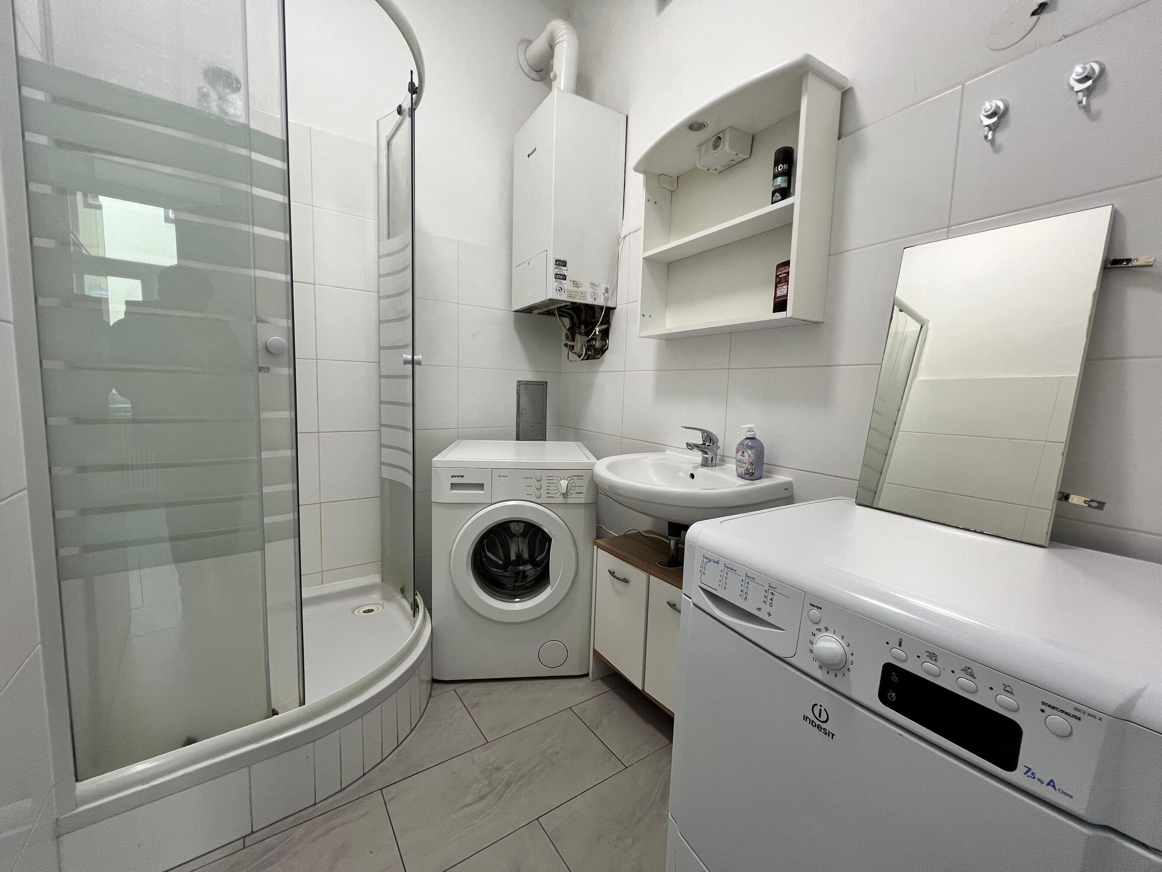 Ein modernes Badezimmer mit Duschkabine aus Glas, integrierter Waschmaschine, Waschbecken und Spiegel.