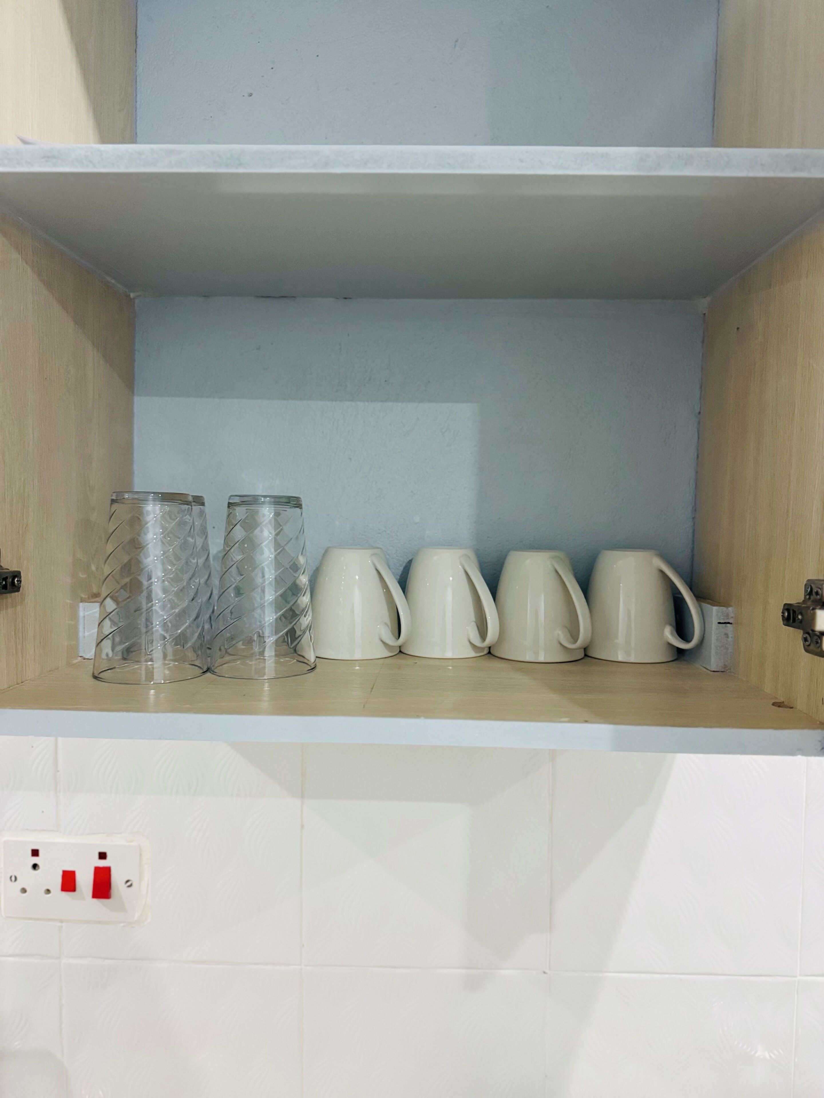 Una estantería de cocina con vasos de vidrio y tazas de cerámica blanca.