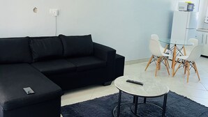 A modern living room with a black sectional sofa, a round coffee table, and a glass dining table with white chairs.