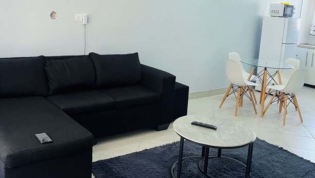 A modern living room with a black sectional sofa, a round coffee table, and a glass dining table with white chairs. - Cozy 2-bedroom 2-bathroom house in charming Mutare with luxury amenities. (Mutare)
