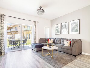 Una sala de estar con un sofá gris, una mesa de centro y un balcón con mobiliario exterior.