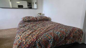 A bed with a patterned bedspread, a bedside lamp, and a mirror on the wall.