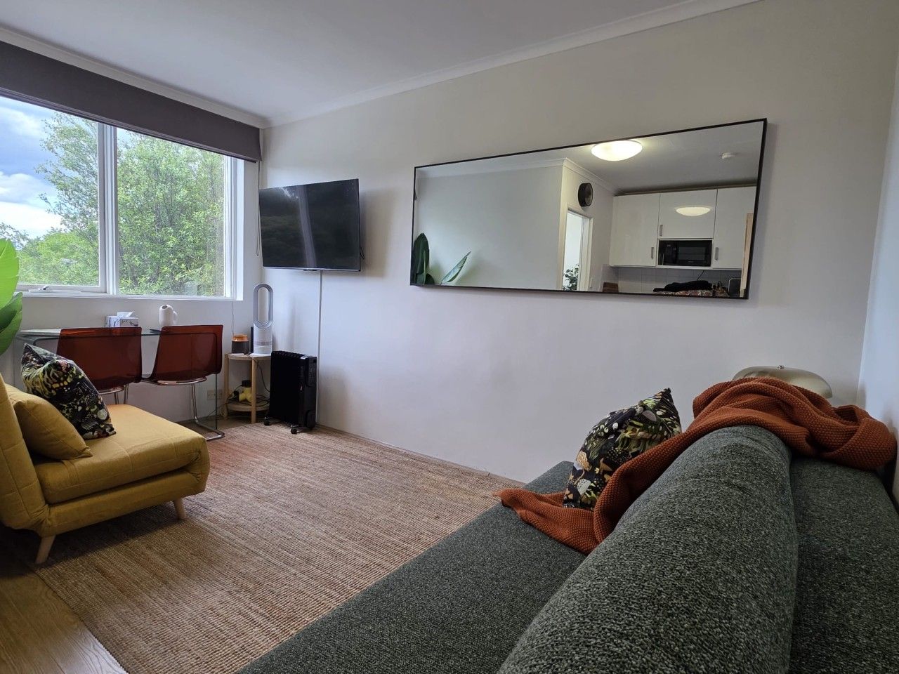 A living room with a sofa, a chair, a television, and a kitchen area visible through a window.