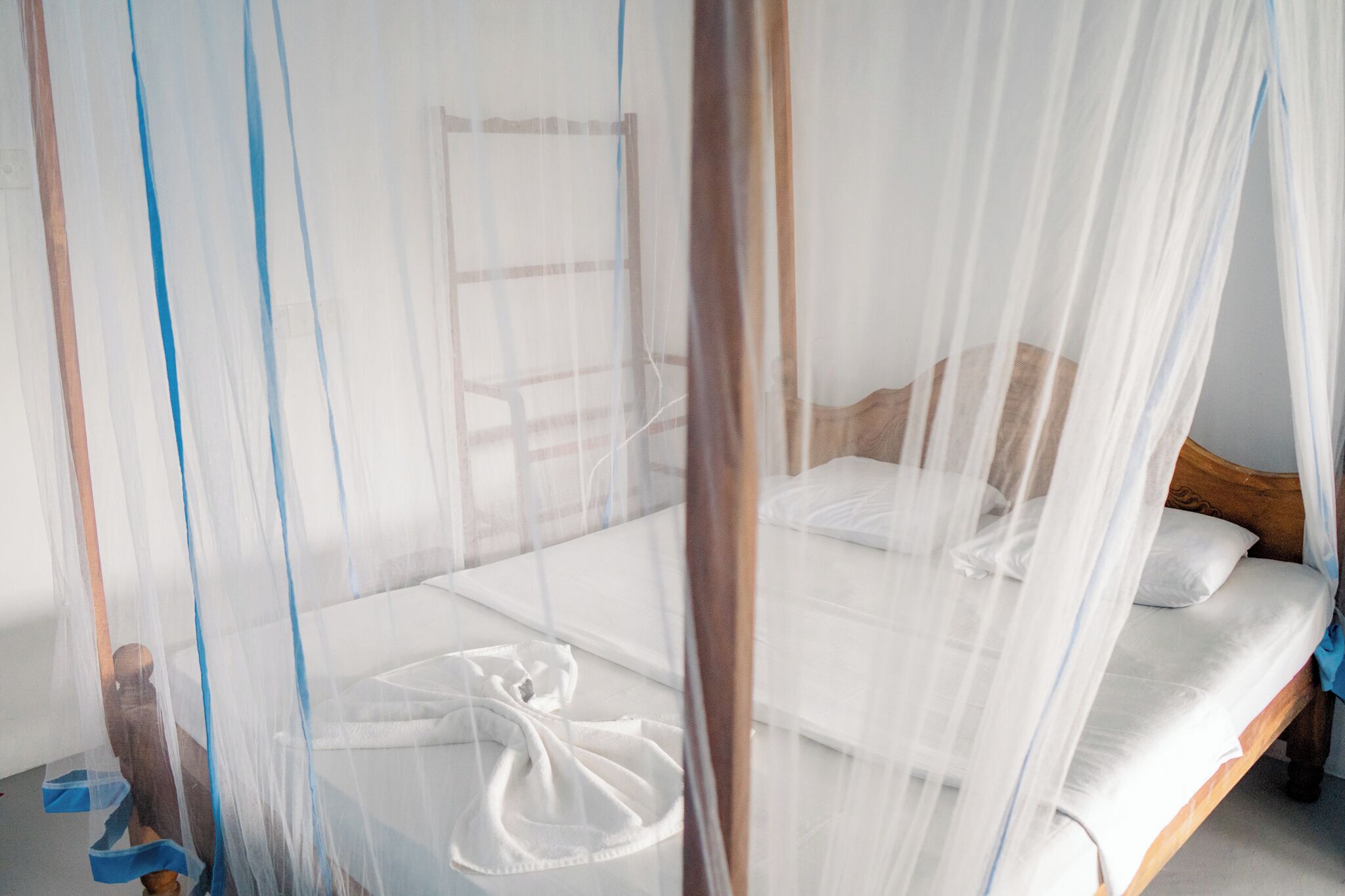 Un dormitorio con una cama cubierta por una mosquitera, cabecera de madera y ropa de cama blanca.