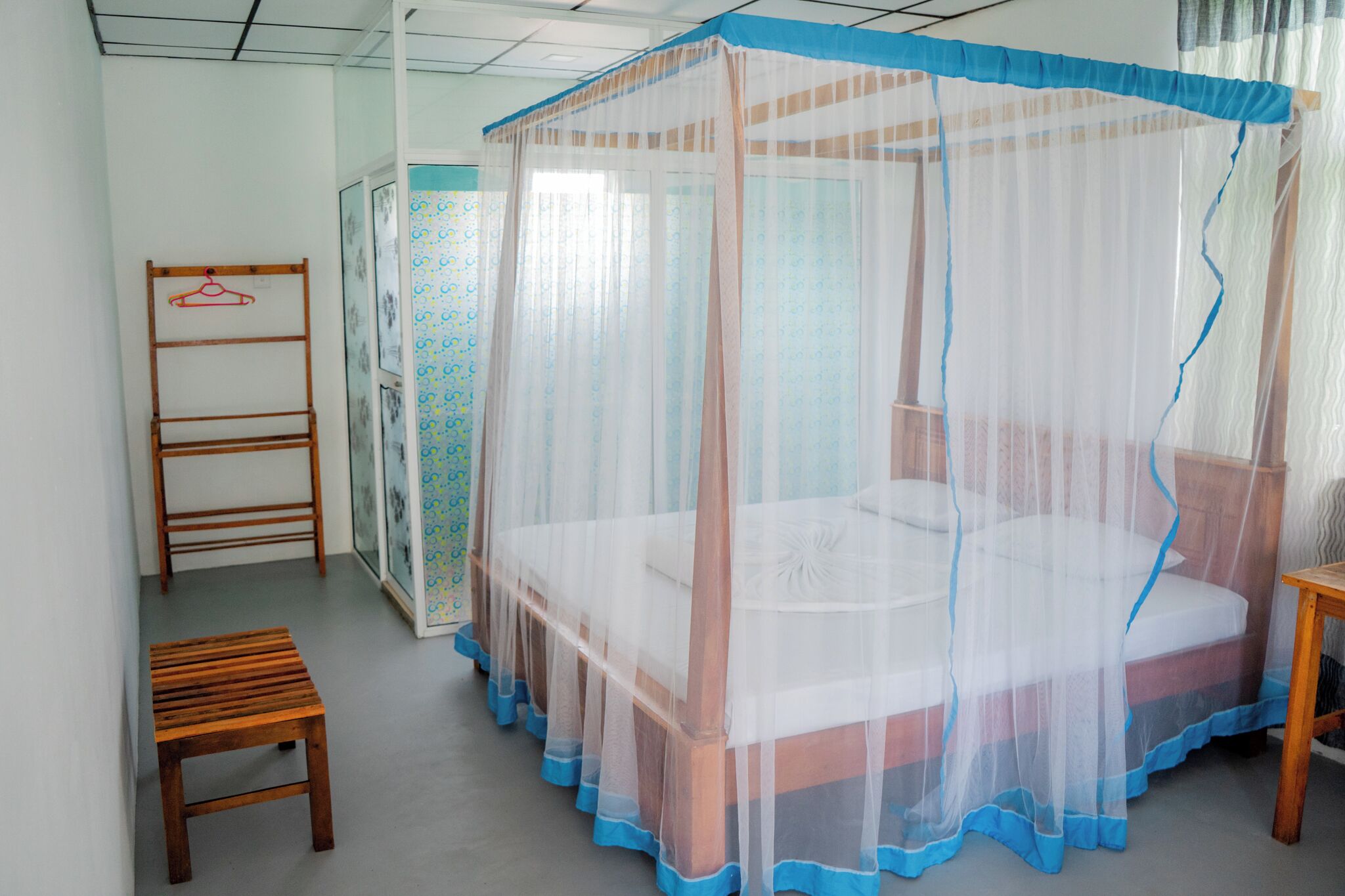 A bedroom with a bed under a mosquito net, a wooden chair, and a wardrobe.