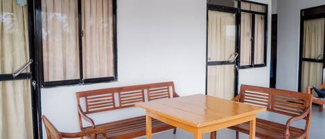 Una habitación con una mesa de madera y bancos, ventanas amplias con cortinas y una pared blanca.