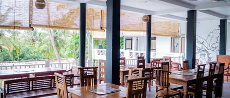 A restaurant with wooden tables and chairs, large windows with a view of palm trees, and a ceiling fan.