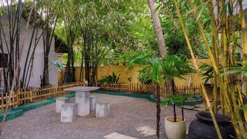 Un patio con una mesa de hormigón rodeado de bloques de piedra, plantas de bambú y una valla de madera.