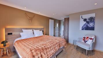 Une chambre avec un grand lit, une tête de lit en bois, une couverture orange moelleuse, une chaise blanche avec un coussin à motif de vache et une décoration murale représentant un crâne de taureau.