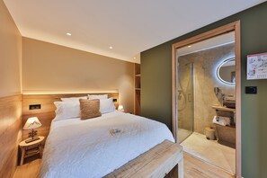 A hotel room with a bed, bedside lamp, wooden headboard, and a shower area with a glass door. - Domaine Le H (Hohrod)