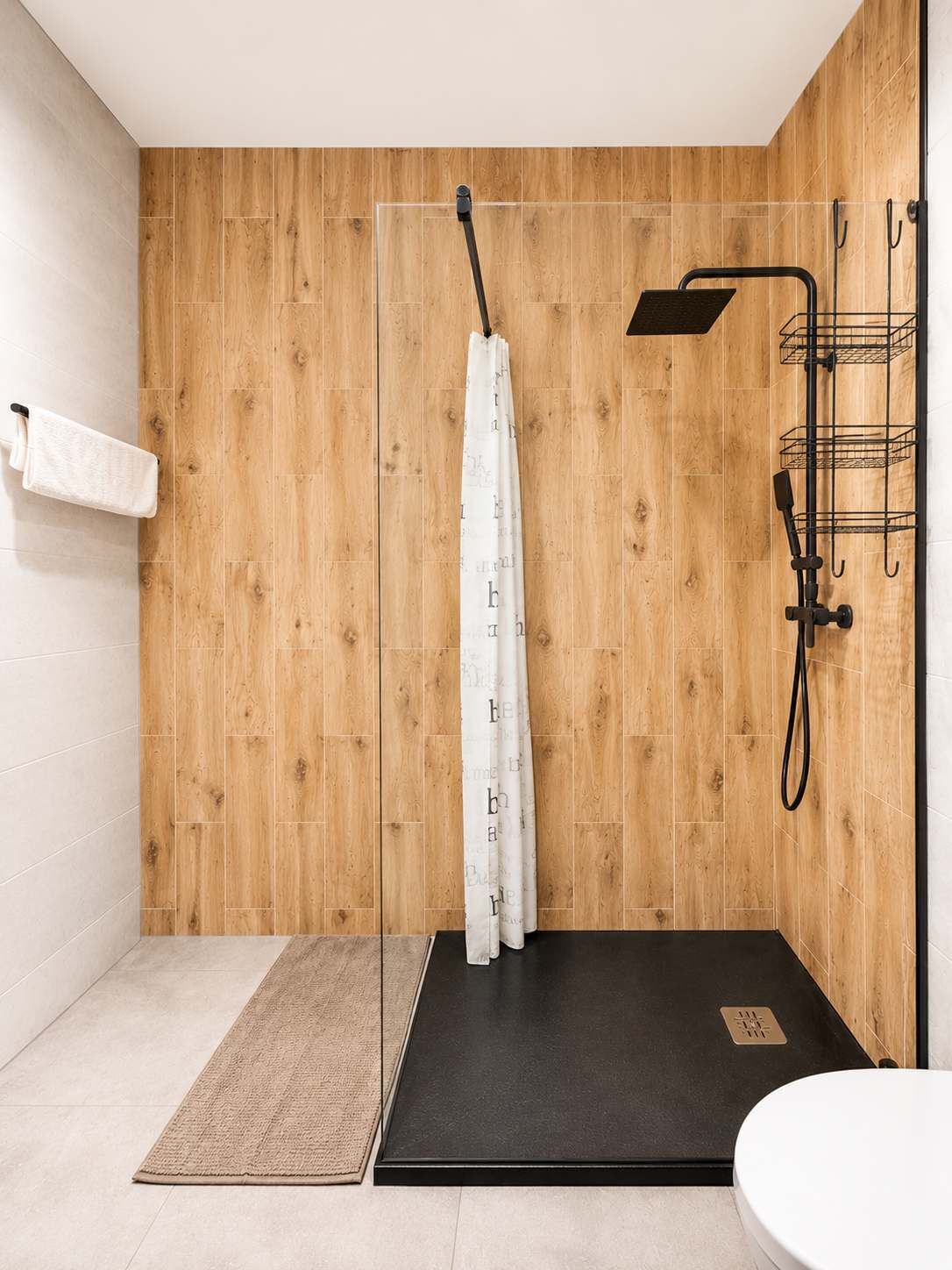 A modern bathroom with a wooden wall, a shower with a black floor, a white towel, and a metal rack.