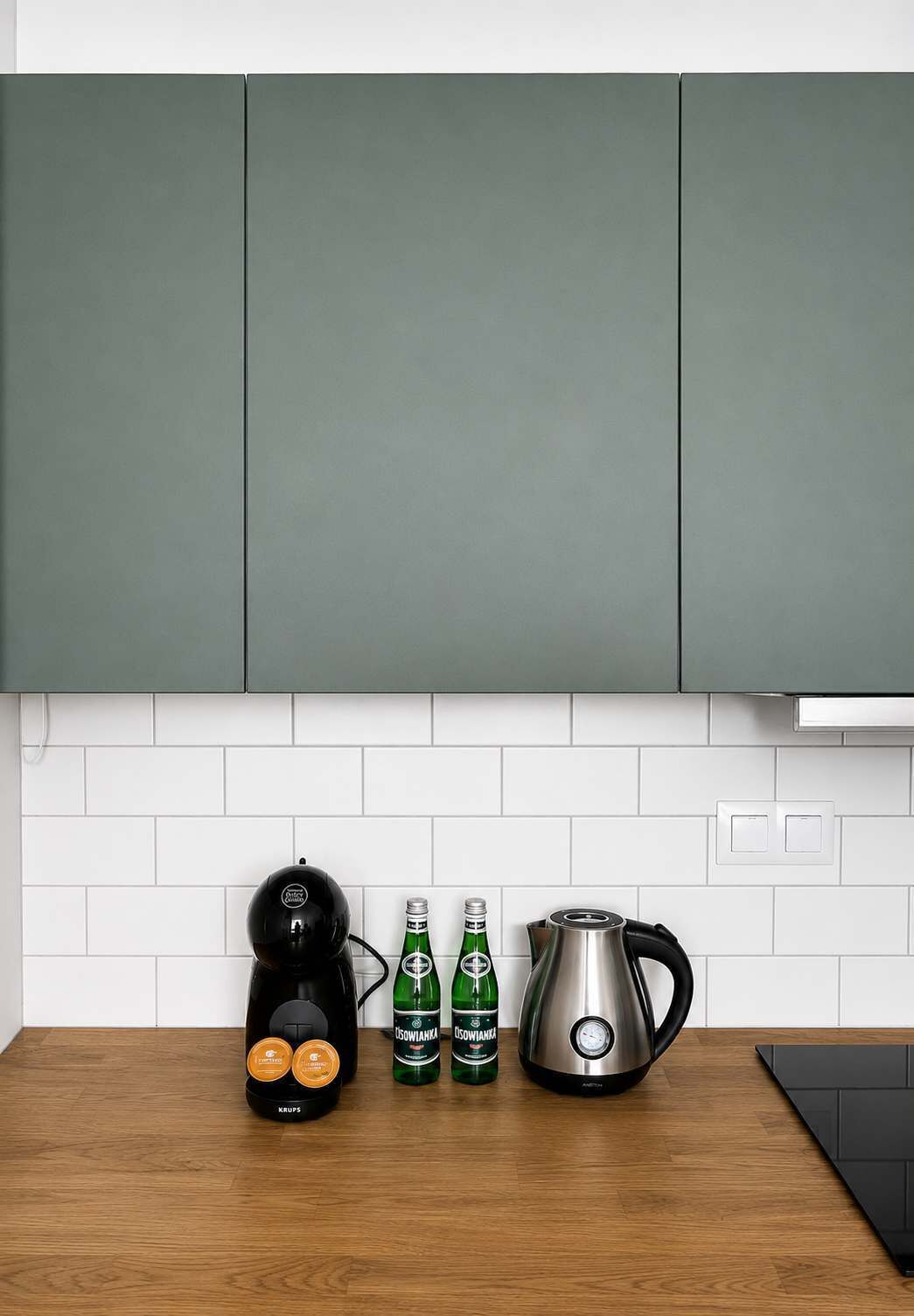 A kitchen with a coffee maker, two bottles of beer, and a kettle on a wooden countertop.