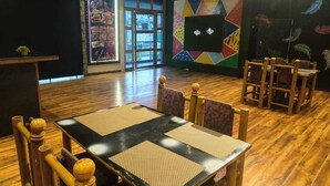 Un restaurante con suelo de madera, una mesa grande con individuales tejidos y un mural de pared geométrico y colorido.