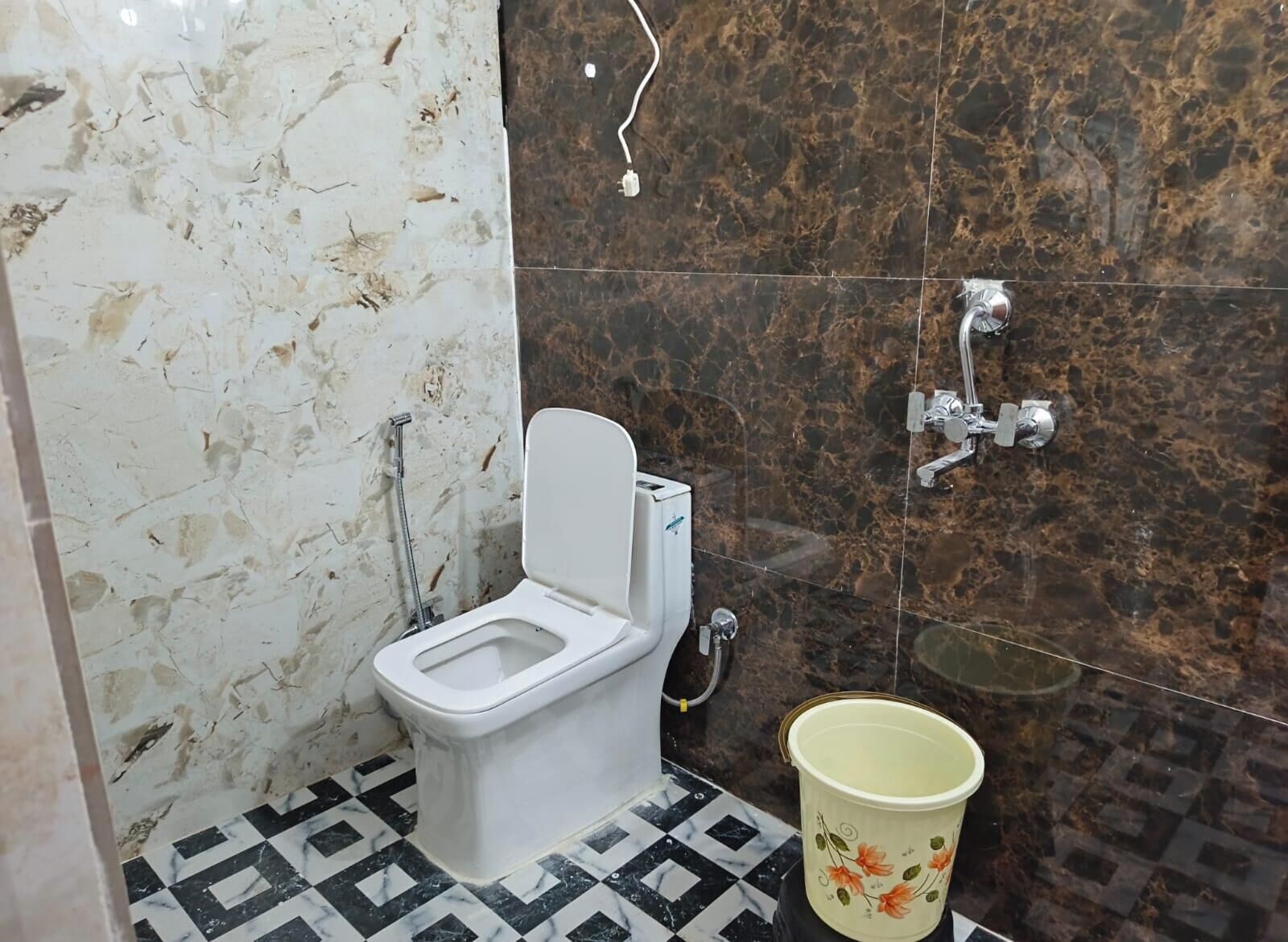 Egy fürdőszoba, amelyben WC, zuhanyzó és vödör található.