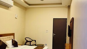 Una habitación de hotel con cama, una silla, una mesita, un ventilador de techo y una puerta.
