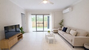 A modern living room with a flat-screen TV, a beige sofa, a coffee table, and a ceiling fan.