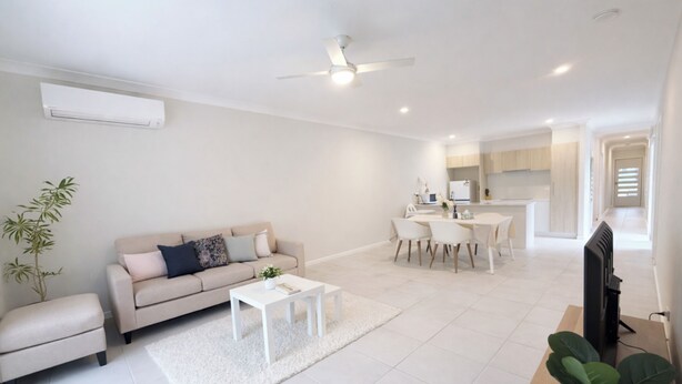 A modern living room with a sofa, coffee table, and a TV. There is a dining area with a table and chairs.
