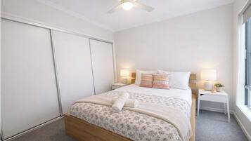 Een slaapkamer met een bed, nachtkastjes, een plafondventilator en een raam.