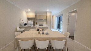 A modern kitchen with white cabinets, a dining table with four chairs, and a vase with flowers.