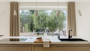 Une cuisine avec une grande fenêtre, un évier, un plan de travail et un saladier rempli de fruits.