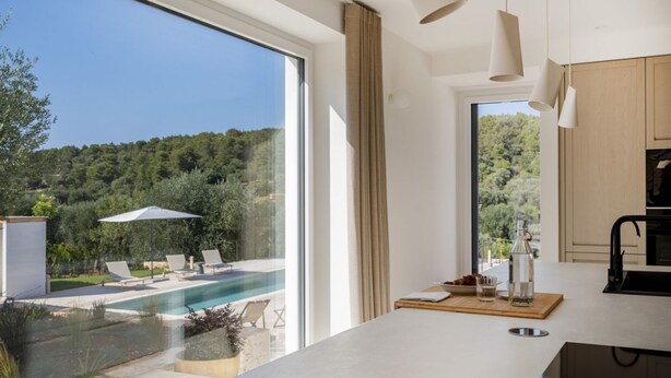 Une cuisine moderne avec une grande fenêtre, une piscine et un espace salon extérieur.