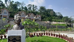 A statue in a garden with a stone pathway, surrounded by potted plants and a stone wall. - Sparsh Himalaya Shivir (Rishikesh)