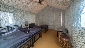 A room with two beds, a small table, a stool, and a ceiling fan. - Sparsh Himalaya Shivir (Rishikesh)