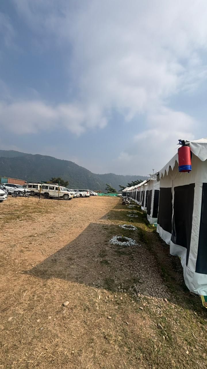 A row of tents with a red water tank on the right, parked on a dirt ground with a mountainous backdrop.