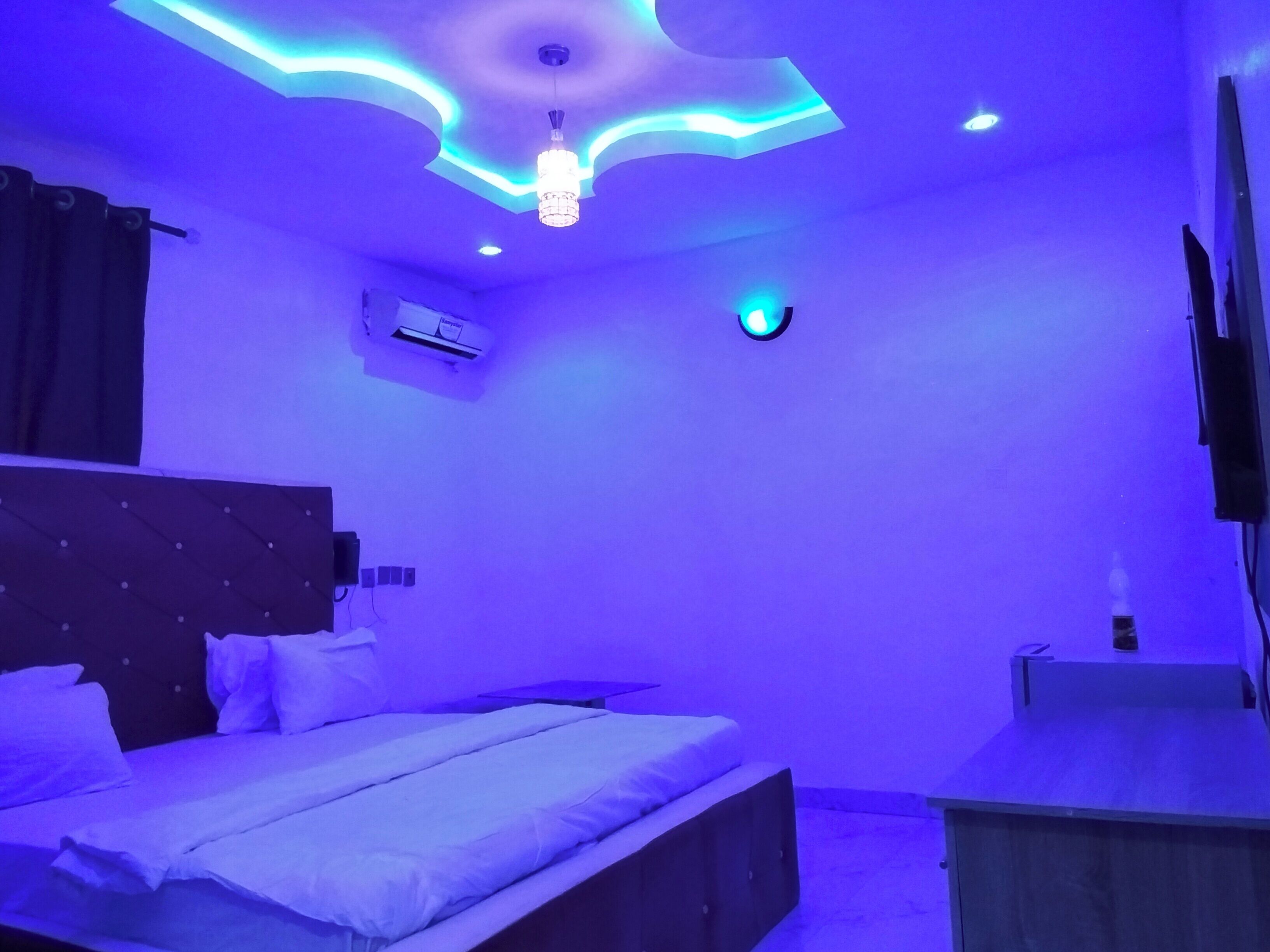 A bedroom with a bed, a nightstand, an air conditioning unit, and a ceiling light fixture.