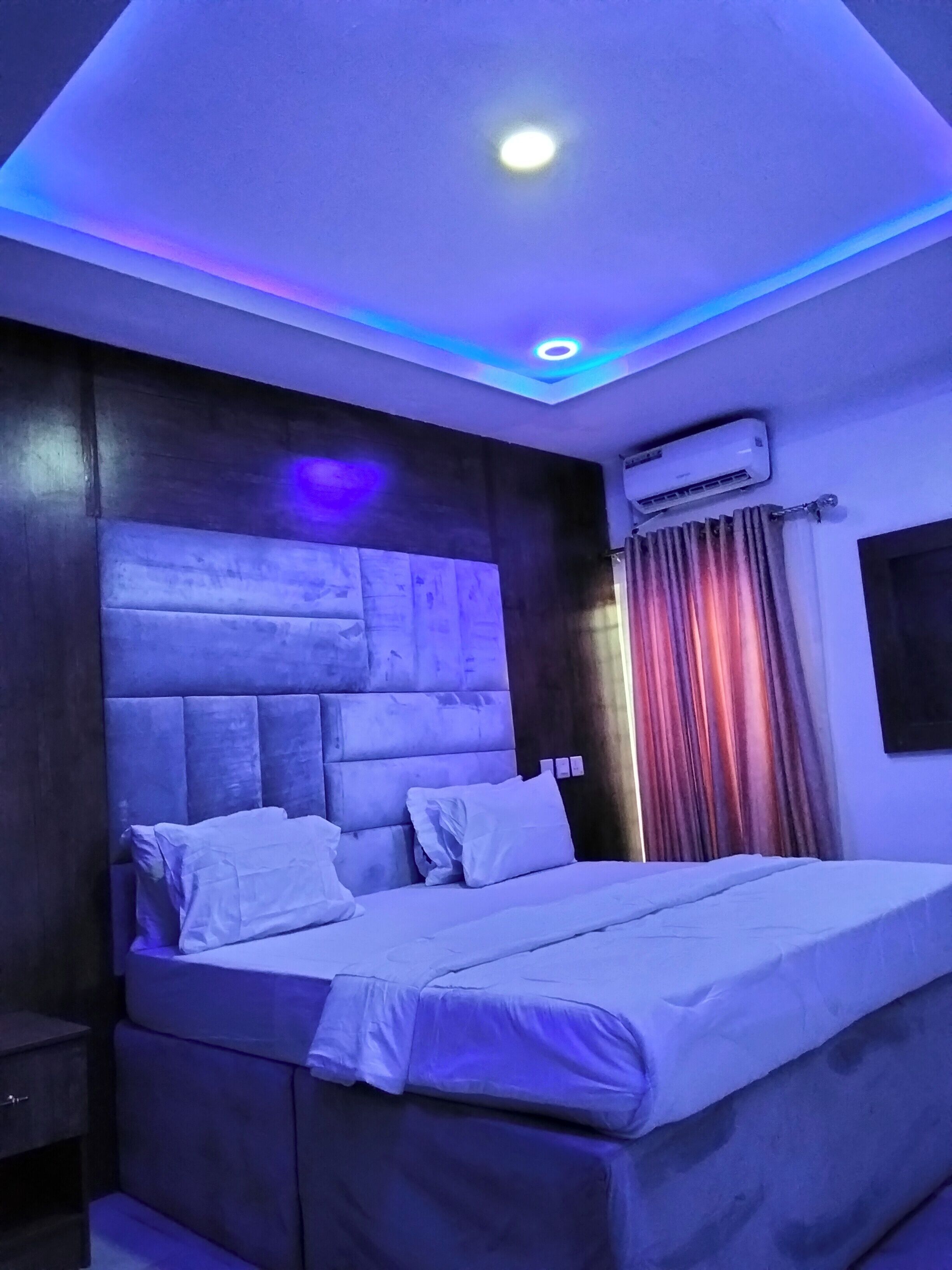 A modern bedroom with a large bed, a headboard with a built-in shelf, and an air conditioning unit on the wall.