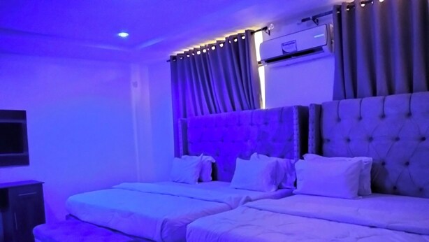 A hotel room with two beds, a flat-screen TV, an air conditioning unit, and a window with curtains. - KINGSAMYSTAR HOTEL AND SUITES  (Asaba)