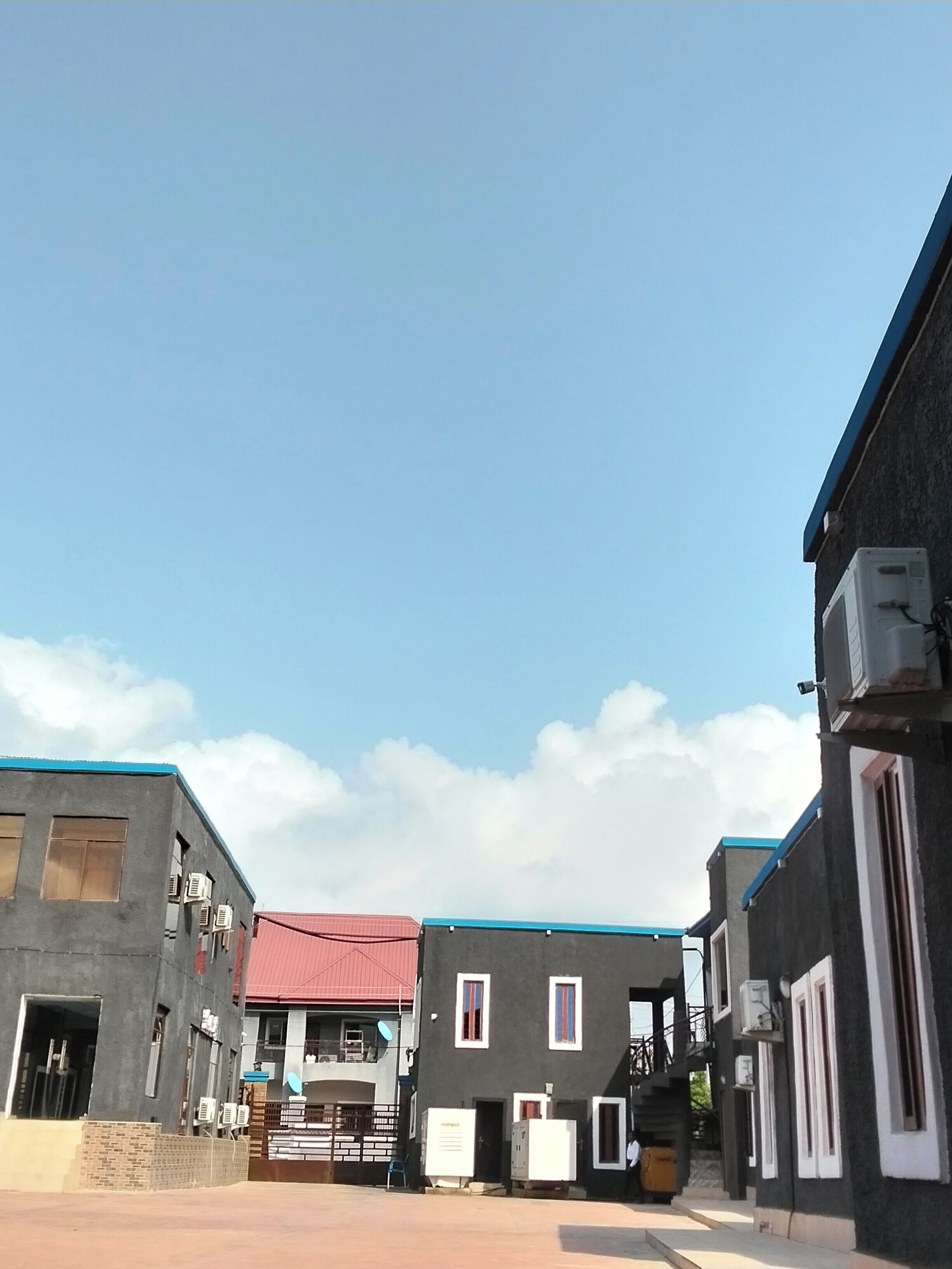 Una calle estrecha flanqueada por edificios, con unidades de aire acondicionado y una estructura de techo rojo.