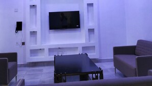 A modern living room with a flat-screen TV mounted on a white wall, surrounded by built-in shelving. There are two sofas and a coffee table in the room. - KINGSAMYSTAR HOTEL AND SUITES  (Asaba)